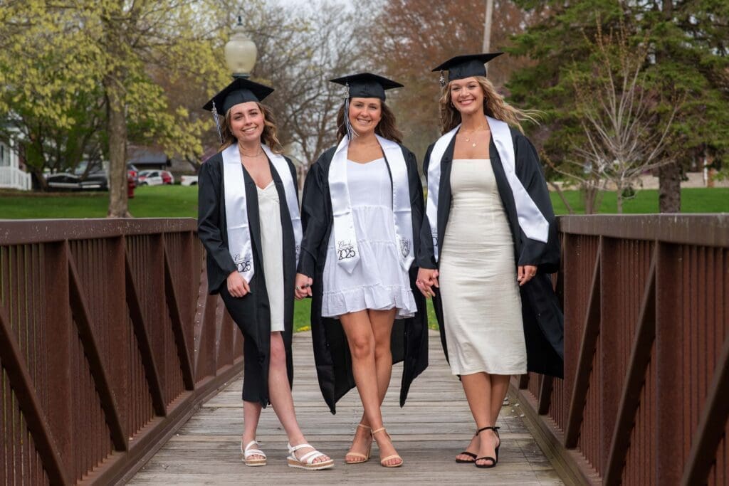 high school senior girls in white dresses with black cap and gowns on a bridge