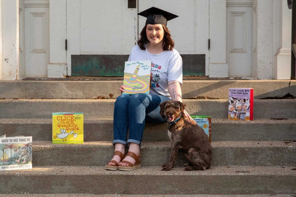 Girl wearing graduation cap with books and dog